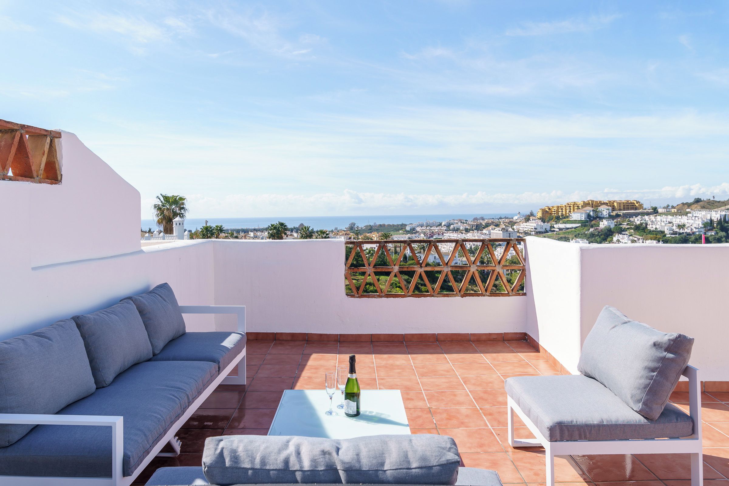 A terrace with a sofa, a chair, and a table with a bottle and glasses.