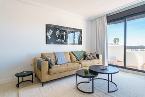 A modern living room with a beige sofa, two black coffee tables, and a large window with a view of the city. - Luxe Golf & Family House Escape (Estepona)