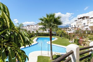 A swimming pool with a palm tree in the foreground, surrounded by a well-maintained lawn and a row of white buildings in the background. - Luxe Golf & Family House Escape (Estepona)