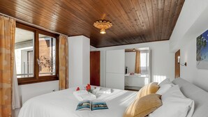 A bedroom with a wooden ceiling, a bed with white bedding, a book, and a window with curtains. - Bel Panorama 2 Ronco Sopra Ascona (Ronco sopra Ascona)
