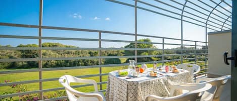 Un balcón con una mesa dispuesta para dos personas, con vista a un paisaje verde.