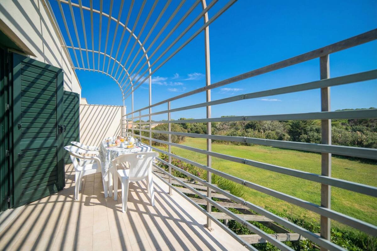 An outdoor terrace with a table and chairs, a view of the countryside, and a metal railing.