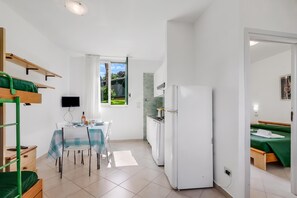 Una habitación de hotel compacta con zona de comedor, kitchenette y cama con colcha verde.