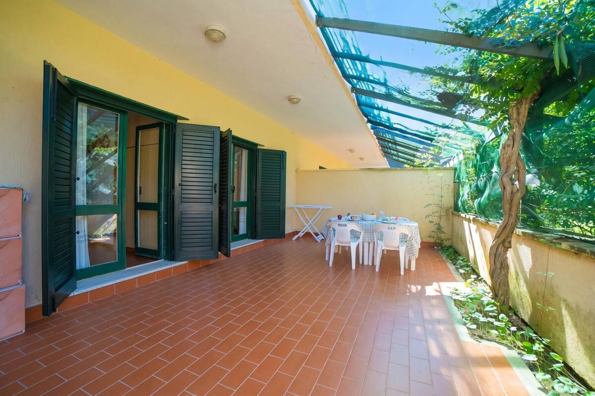 A covered patio with a tiled floor, a table with chairs, and a small table with a tablecloth.