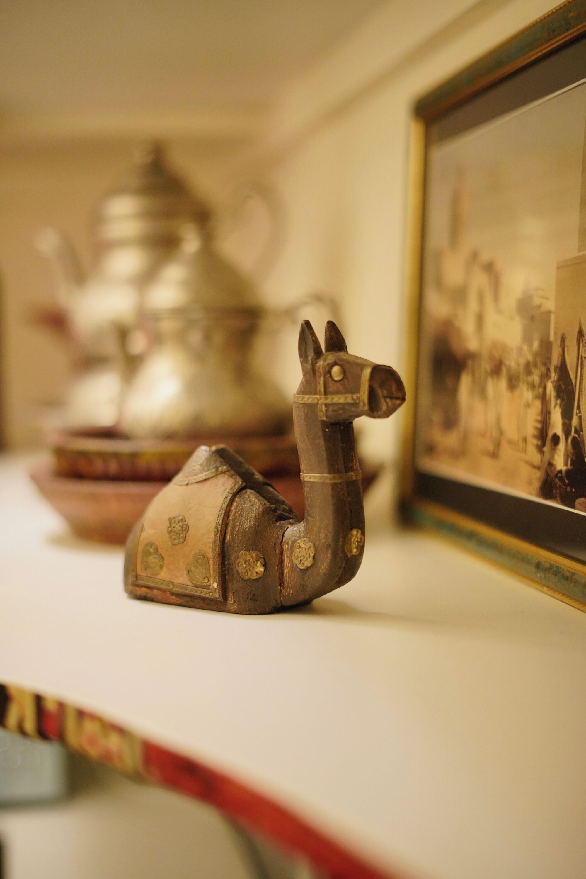 Een plank met een decoratief keramieken lama beeldje, een zilveren theepot en een ingelijste foto.