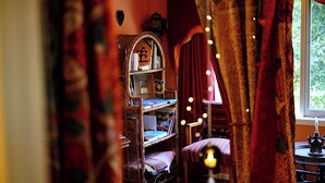 A cozy reading nook with a wicker bookshelf, a cushioned chair, and a small table with a candle.