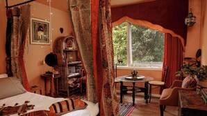 A bedroom with a bed, a small round table, a chair, and a window with curtains.