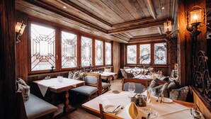 A restaurant with wooden interiors, multiple tables, and chairs, and large windows with geometric stained glass.