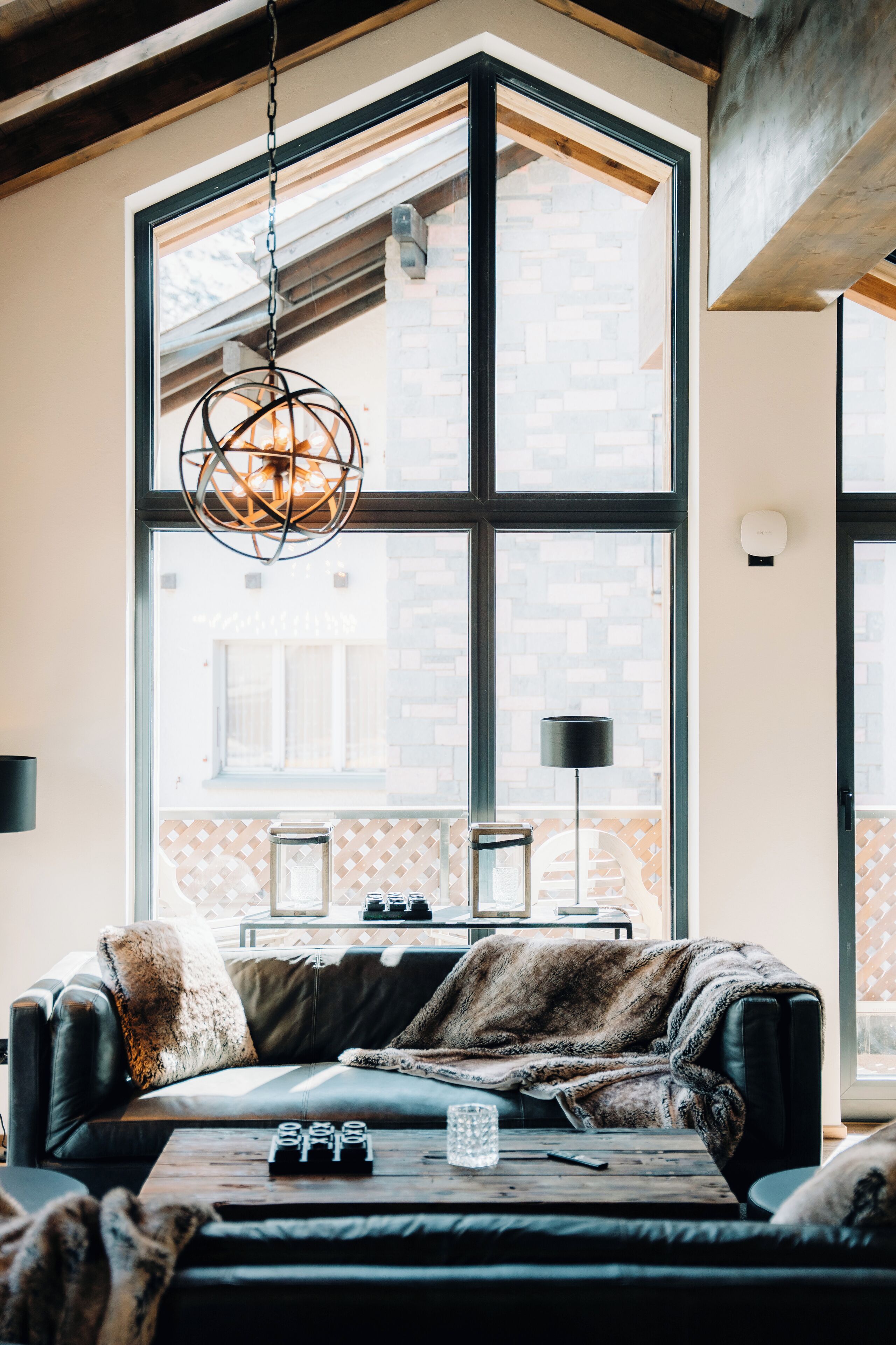 Ein modernes Wohnzimmer mit großem Fenster, einer Pendelleuchte, einer Couch, einem Couchtisch und einer durch das Fenster sichtbaren Ziegelwand.