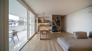 A modern living room with a sofa, dining table, and chairs. There is a kitchen area with a dining table and chairs. The room has large windows and a view of the outside. - CaNova (Spinea)
