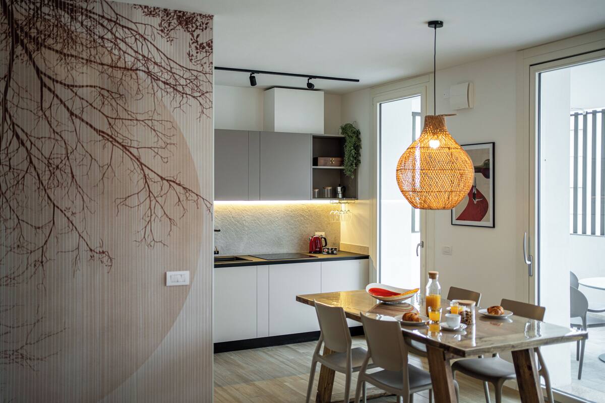 A modern kitchen with a dining area, featuring a wooden table, chairs, and a hanging light fixture.