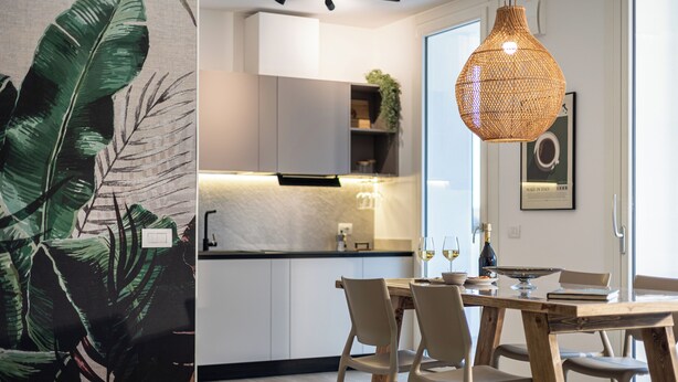 A modern kitchen with white cabinets, a wooden dining table, and a hanging light fixture. - CaNova (Spinea)
