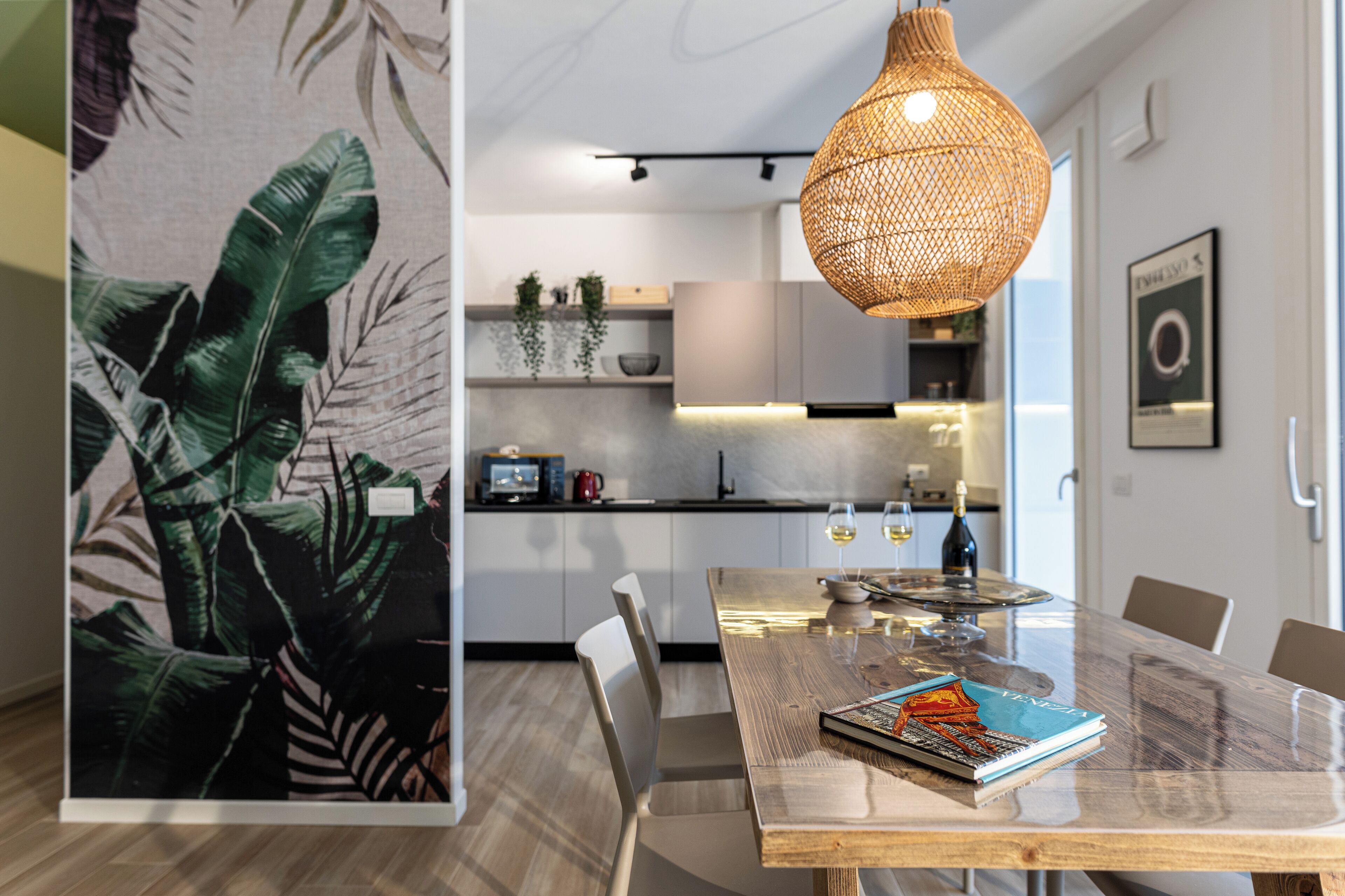 A modern kitchen with white cabinets, a wooden dining table, and a hanging light fixture.
