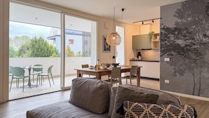 A modern living room with a sofa, a dining area with a table and chairs, and a kitchen in the background. - CaNova (Spinea)