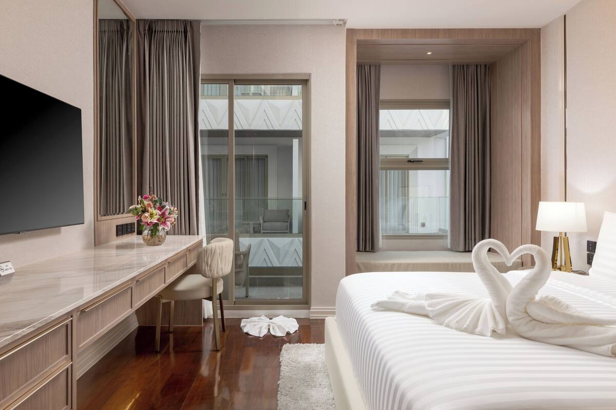 A hotel room with a bed, a desk, a TV, and a view of the outside.