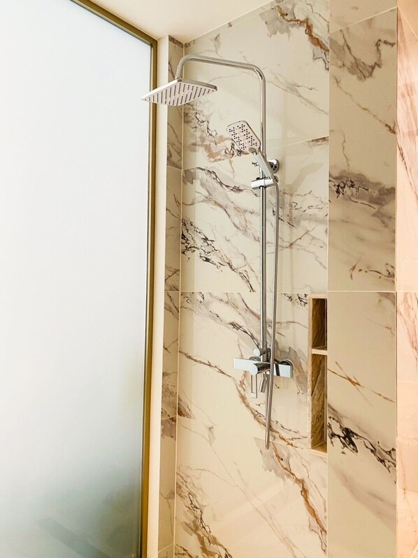 A shower with a handheld showerhead and a wall-mounted rain showerhead, set against a marble wall.