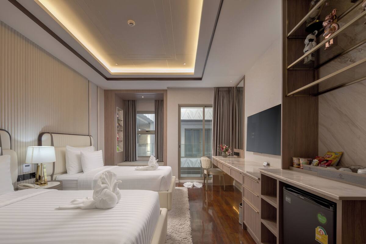A hotel room with two beds, a desk, a refrigerator, and a view of the outdoors.