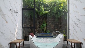 A modern bathroom with a glass-enclosed bathtub, two wooden stools, and a large window with a view of greenery. - LA PLANTE SIEM REAP (Siem Reap)