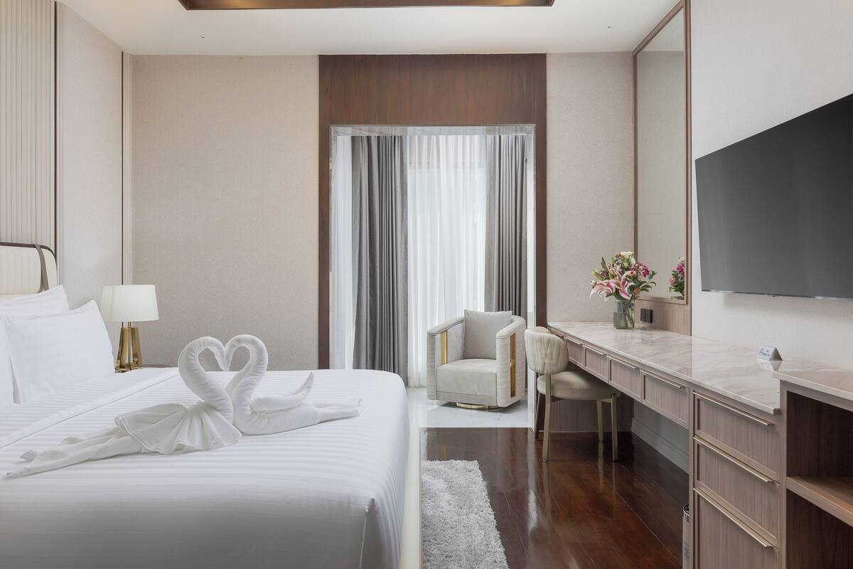 A hotel room with a large bed, a desk, a chair, a TV, and a window with curtains.