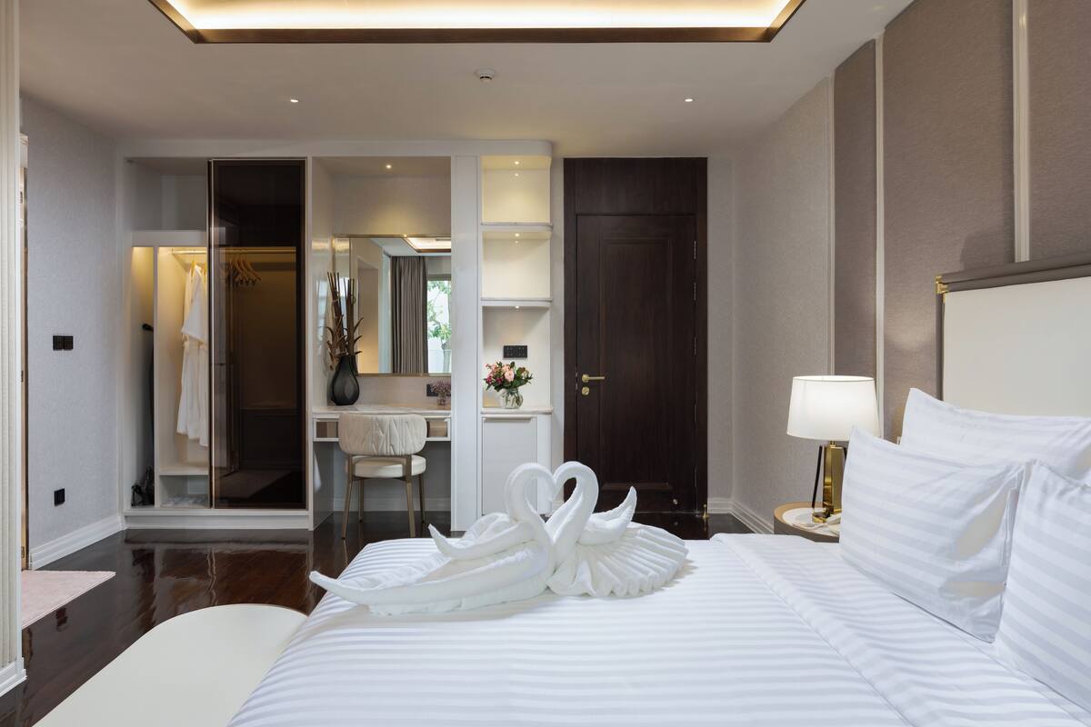 A hotel room with a large bed, a bedside table with a lamp, a wardrobe, and a bathroom visible through an open door.