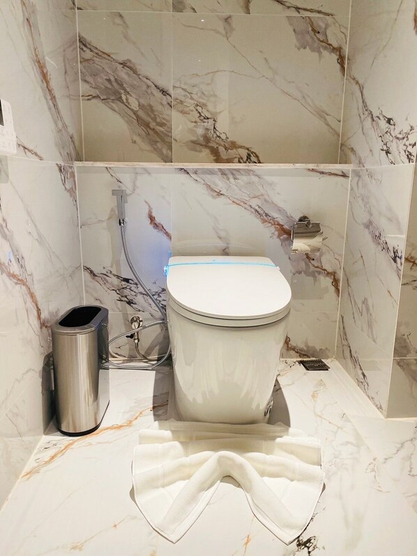 A bathroom with a toilet, a trash can, and a towel on the floor.