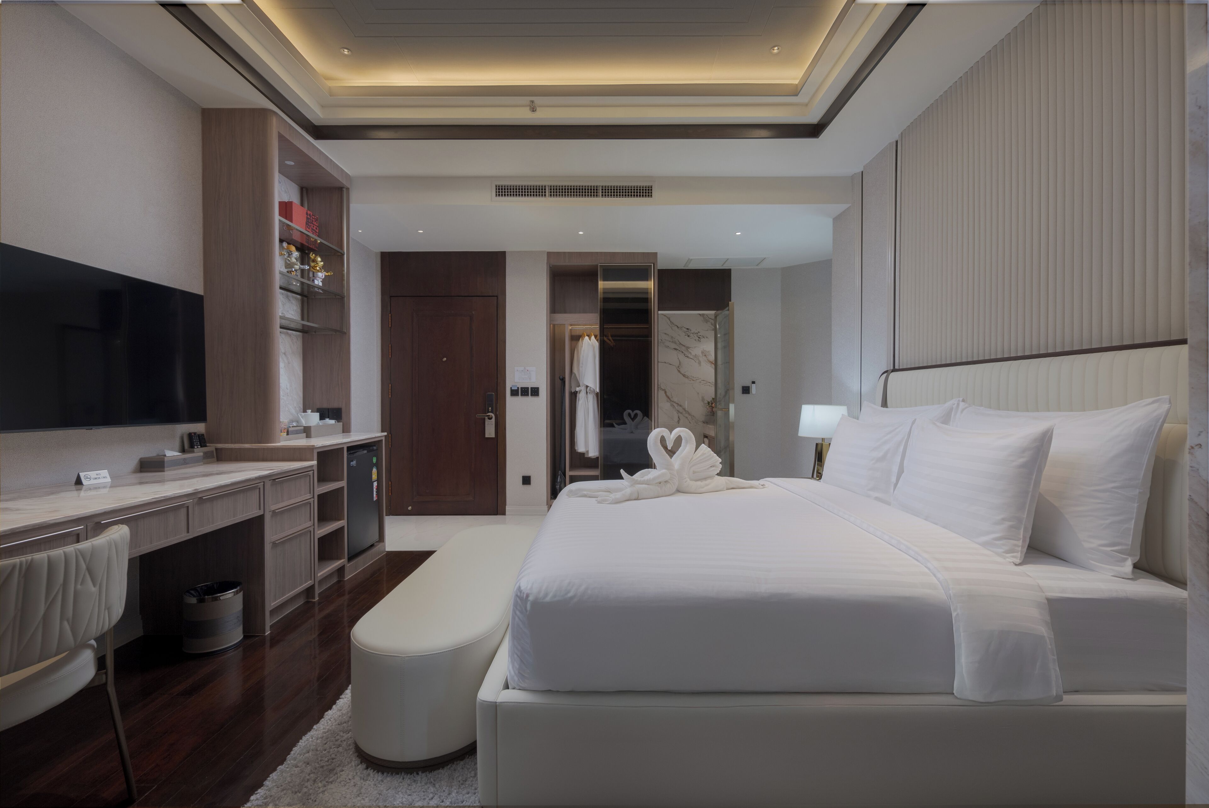 Une chambre d’hôtel moderne dotée d’un grand lit, d’un bureau avec un téléviseur à écran plat, d’une coiffeuse avec un miroir et d’un dressing.