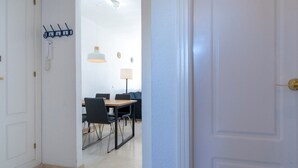 A hallway leading to a dining area with a table and chairs, a lamp, and a coat rack. - Riviera Golf Apartment - Pool Views!  - Pass the Keys (Urbanización Riviera Sol)