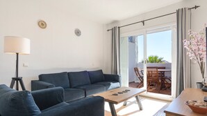 A modern living room with a sofa set, a coffee table, and a lamp. There is a balcony with a table and chairs. - Riviera Golf Apartment - Pool Views!  - Pass the Keys (Urbanización Riviera Sol)