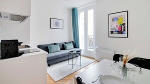 A modern apartment with a kitchenette, a dining area, and a living room with a sofa and a large window with curtains. - Charming studio - 2P- Nanterre (Nanterre)
