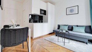 A modern living room with a grey sofa, a black chair, and a small round table. - Charming studio - 2P- Nanterre (Nanterre)