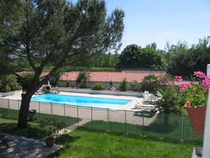 A swimming pool with a fence, a tree, and a building with a red-tiled roof in the background. - Les Garbustets Vacation Home: Group Rental for 15 People Near Fronton with a Pool (Castelnau-d'Estrétefonds)