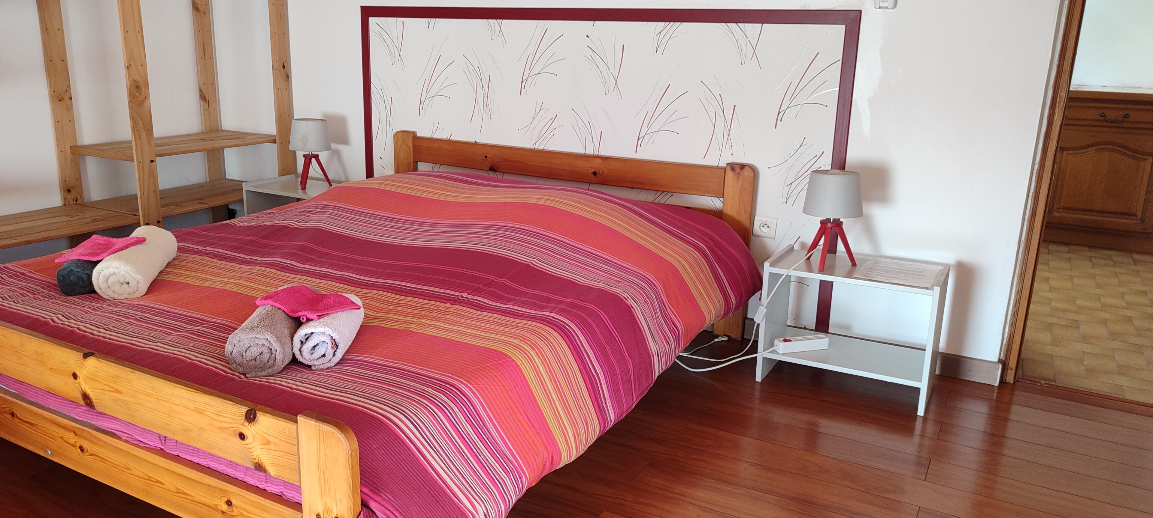 A bed with a striped blanket, two rolled towels, a bedside lamp, and a nightstand with a lamp.