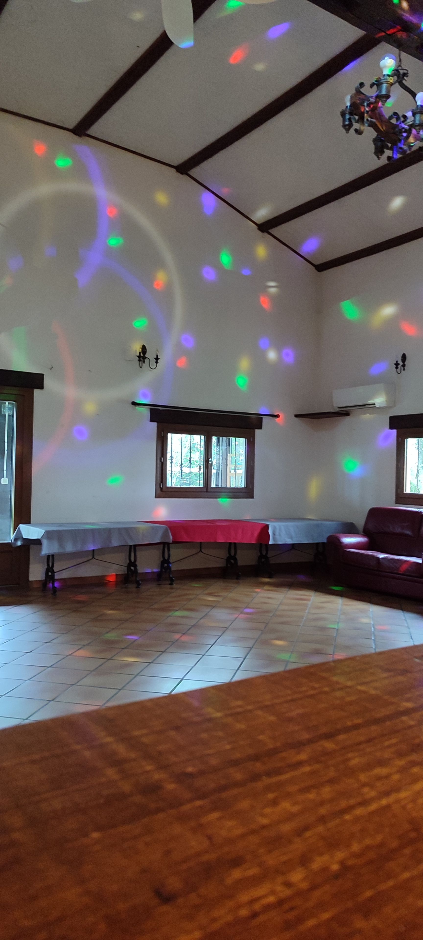 A room with a wooden floor, a table with a red tablecloth, a window with bars, and a chandelier.