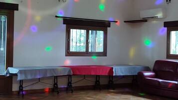 A room with a wooden floor, a table with a red tablecloth, a window with bars, and a chandelier.