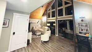 A spacious living room with a high ceiling, a large window, and a cozy seating area.