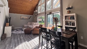 A spacious loft with a high ceiling, large windows, a cozy seating area, and a dining table.