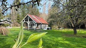 A rustic house with a red roof and white walls, surrounded by lush green grass and trees.