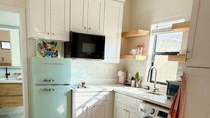 Cocina compacta con armarios blancos, microondas integrado, lavadora y una pequeña mesa de comedor.