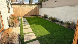 Un patio trasero con césped cuidado, valla de madera y pared de ladrillo blanco.