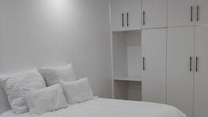 Un dormitorio con cama, ropa de cama blanca y un armario con varias puertas.