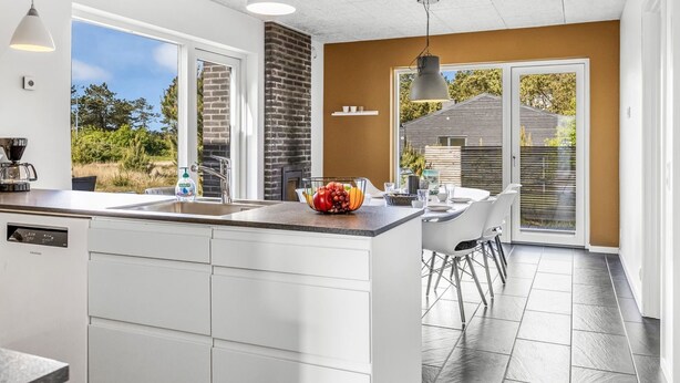 Een moderne keuken met een groot schiereiland, witte kasten en uitzicht op het buiten.