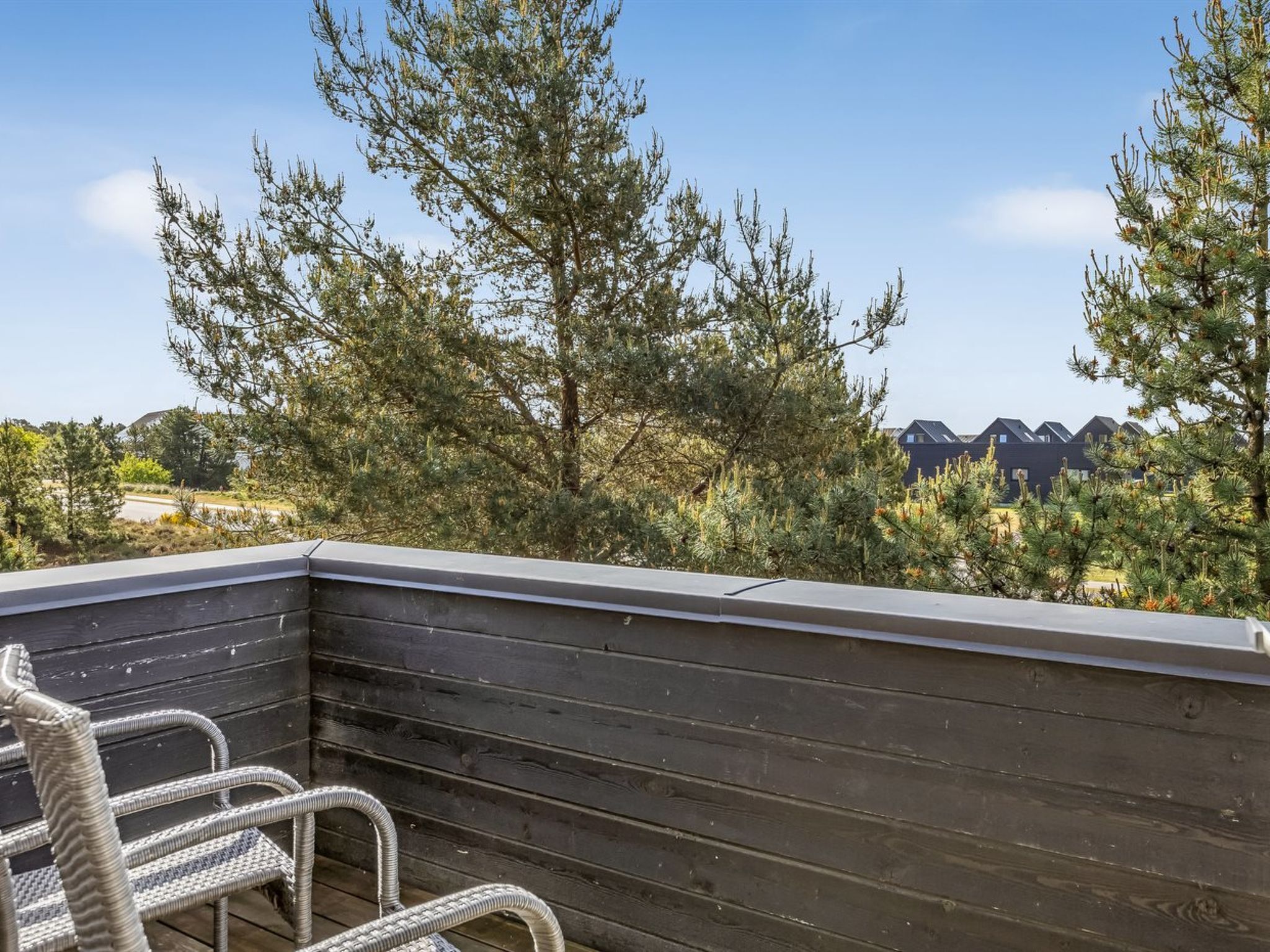 A wooden deck with a wicker chair, overlooking a landscape with trees and a distant building.