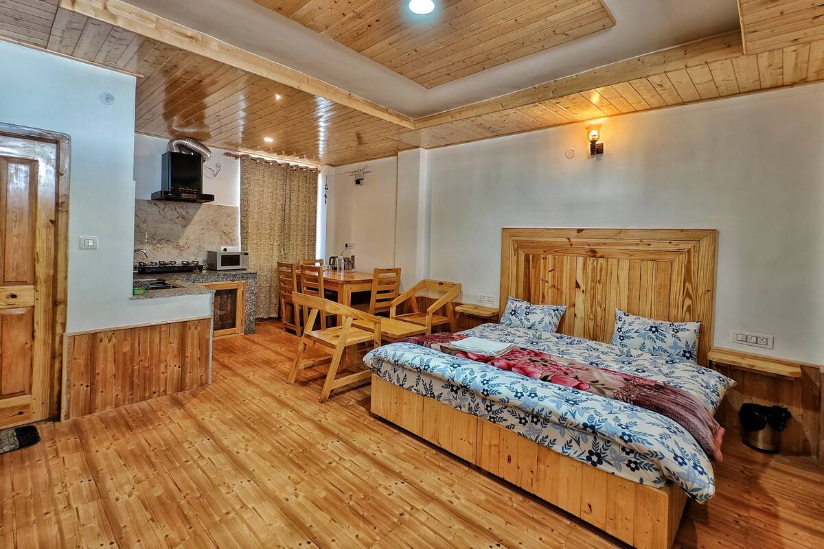 A room with a wooden bed, a dining table, and a kitchen area.