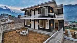 Une maison moderne à deux étages, dotée d’un balcon et entourée d’un paysage montagneux.