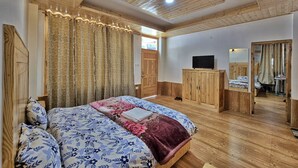 Une chambre avec un plafond en bois, un lit recouvert d’une literie à motifs floraux, une armoire et un téléviseur.