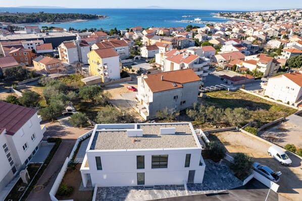 A residential area with a mix of modern and traditional architecture, featuring a prominent white building with a flat roof and a paved driveway.