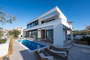 A modern two-story house with a swimming pool and sun loungers.