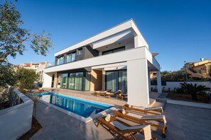 A modern two-story house with a swimming pool, large windows, and outdoor seating.