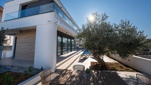 Une maison moderne avec une piscine, un espace salon extérieur et un grand arbre.