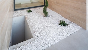 Un intérieur moderne avec une porte en verre donnant sur une salle de bain, un mur en bois et un chemin de gravier agrémenté de petites plantes.